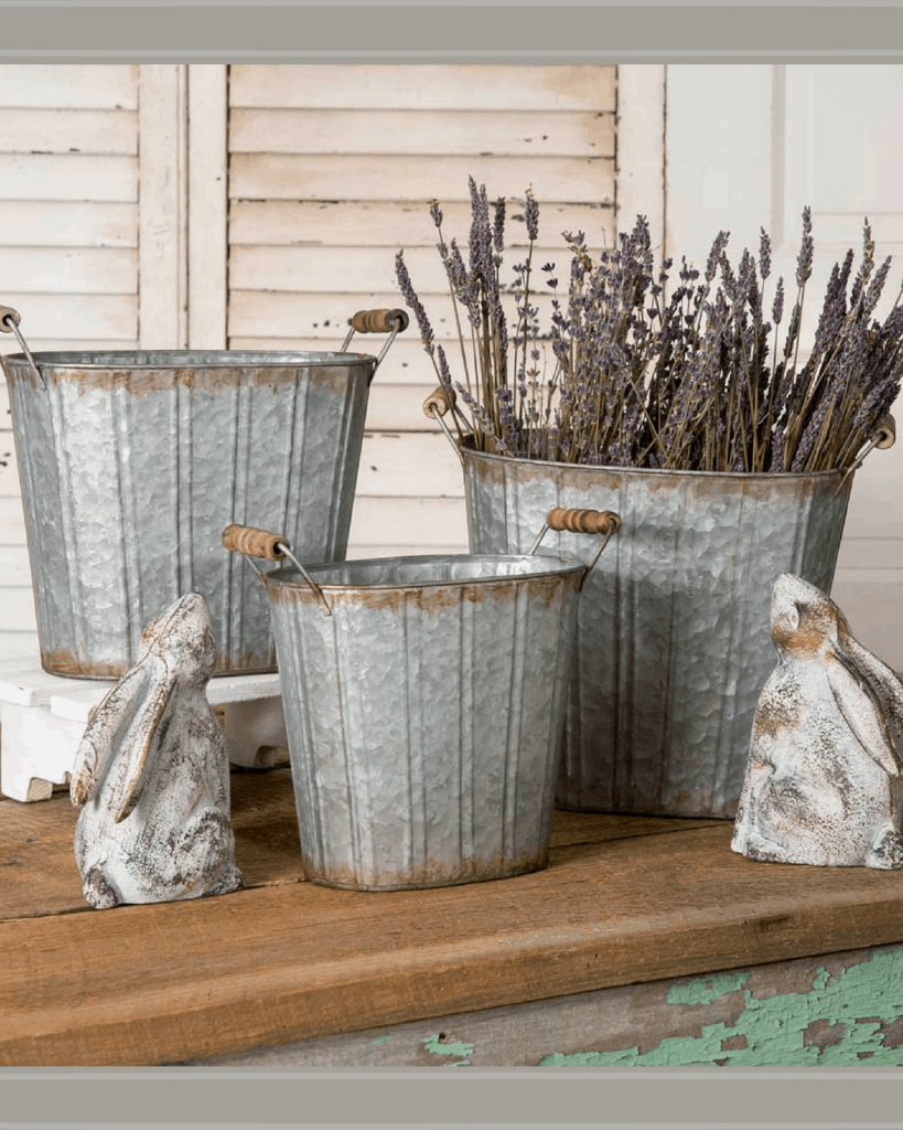 3 galvanized buckets on the porch with lilac in one of them.