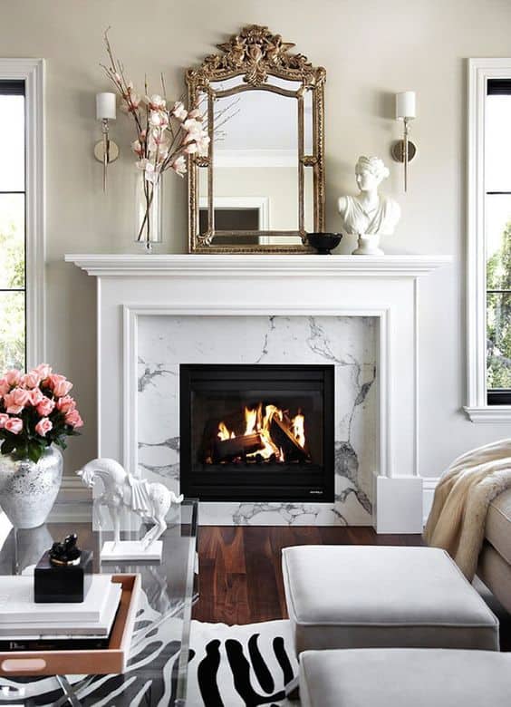 White and marble fireplace with a French inspired mirror above it, and wall sconces flanking the mirror.