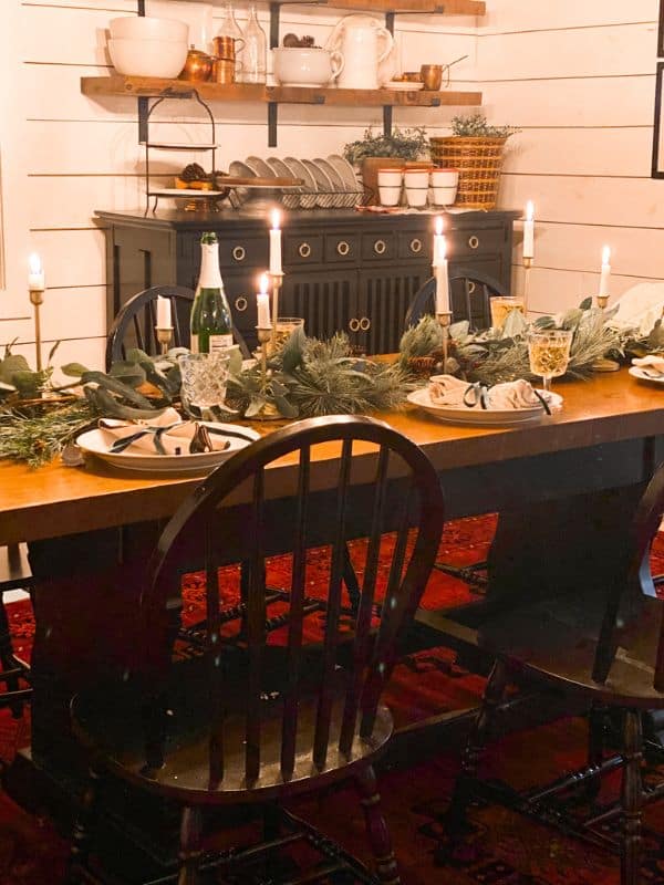 Christmas table set with real fresh garland, plates with rapines and ribbon on top, and lighter taper candles down the center.