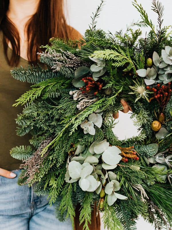 Woman holding a fresh Christmas wreath with berries, ever green, and eucalyptus.