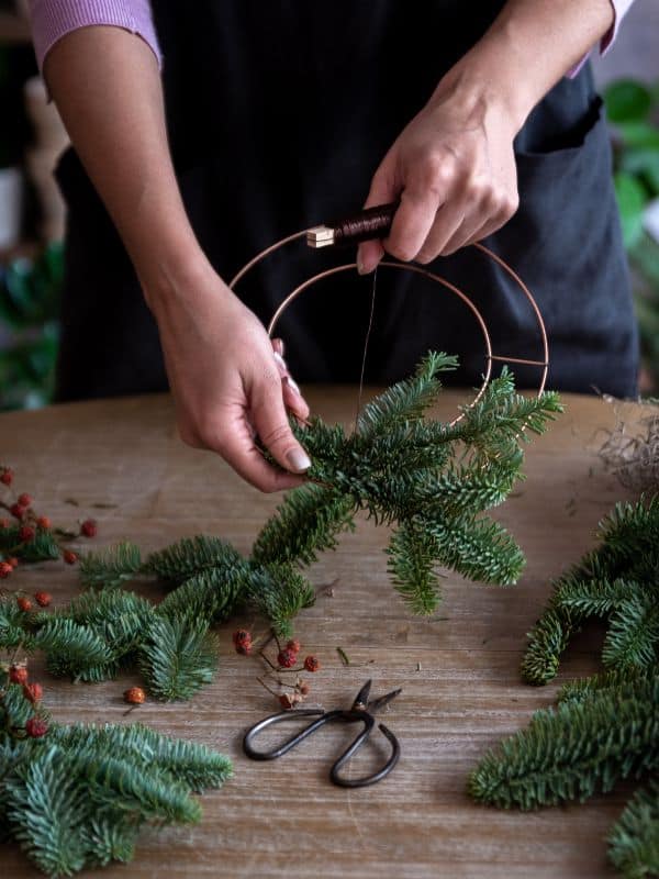 Woman making a wreath from a. metal base with fresh ever green trimmings.