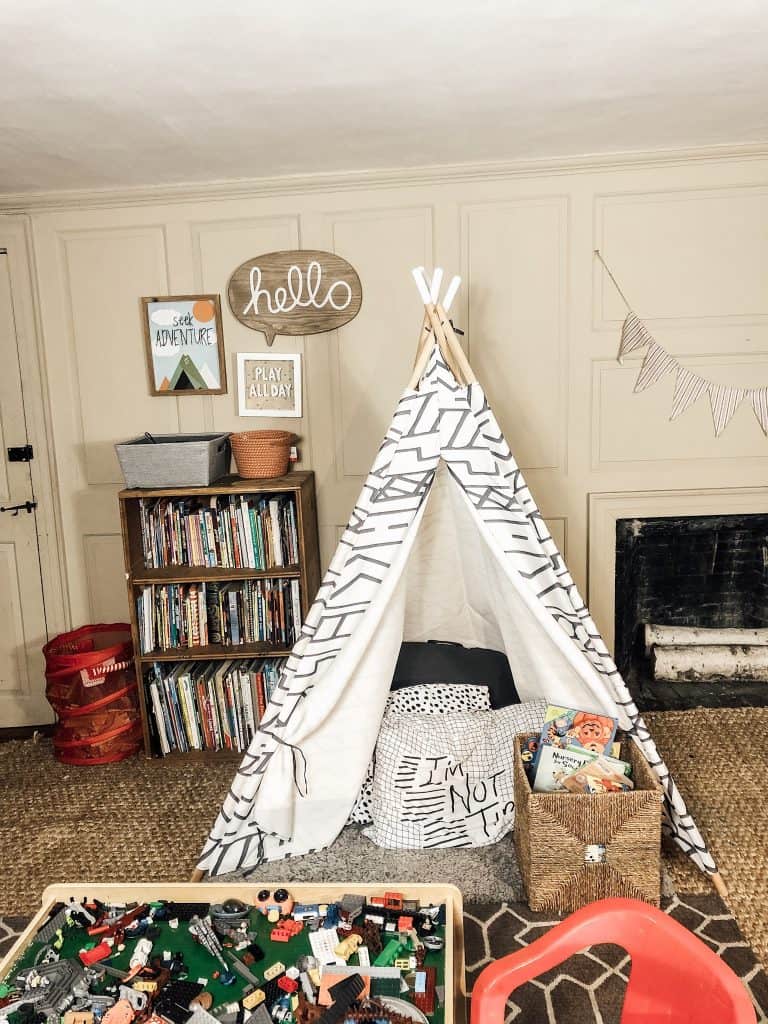 A boys bedroom with a small teepee tent in the middle of the room.  There is a bookshelf behind the tent and also a fireplace in the room.