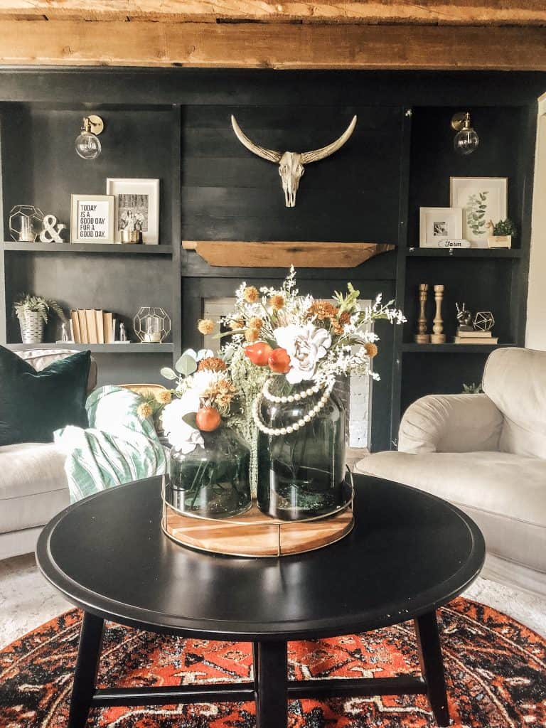 A fall floral arrangement with white, orange flowers on a coffee table in a farmhouse living room.