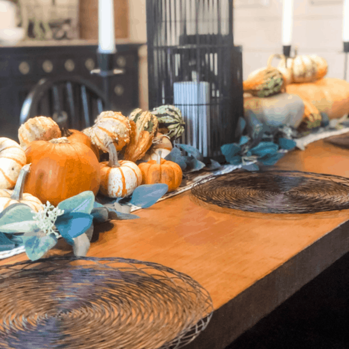 Pumpkins all lined up in the center of a wooden table with a candle in the middle.