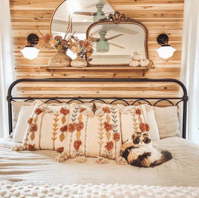 A wrought iron bed with floral pillows and a cat lying on the bed.
