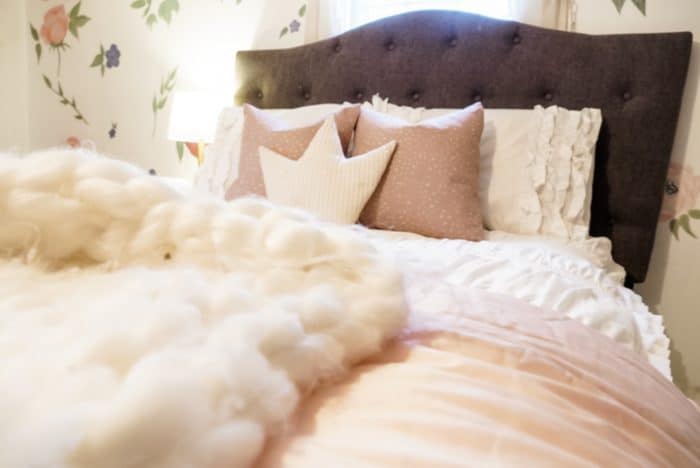White fluffy blanket on the bed with pillows and floral wallpaper.