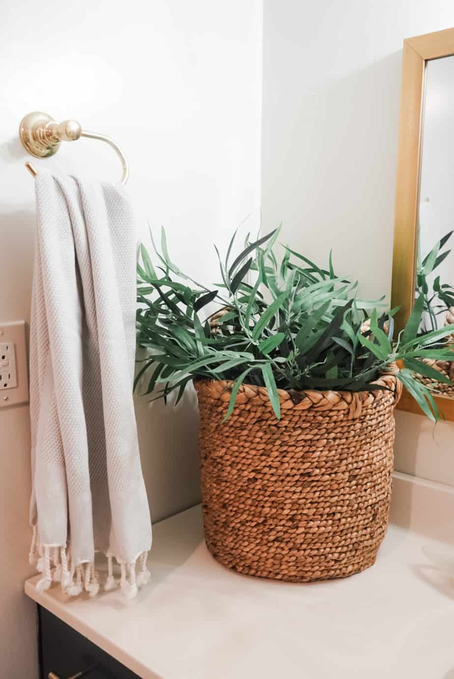 There is a basket filled with a plant on the bathroom counter.