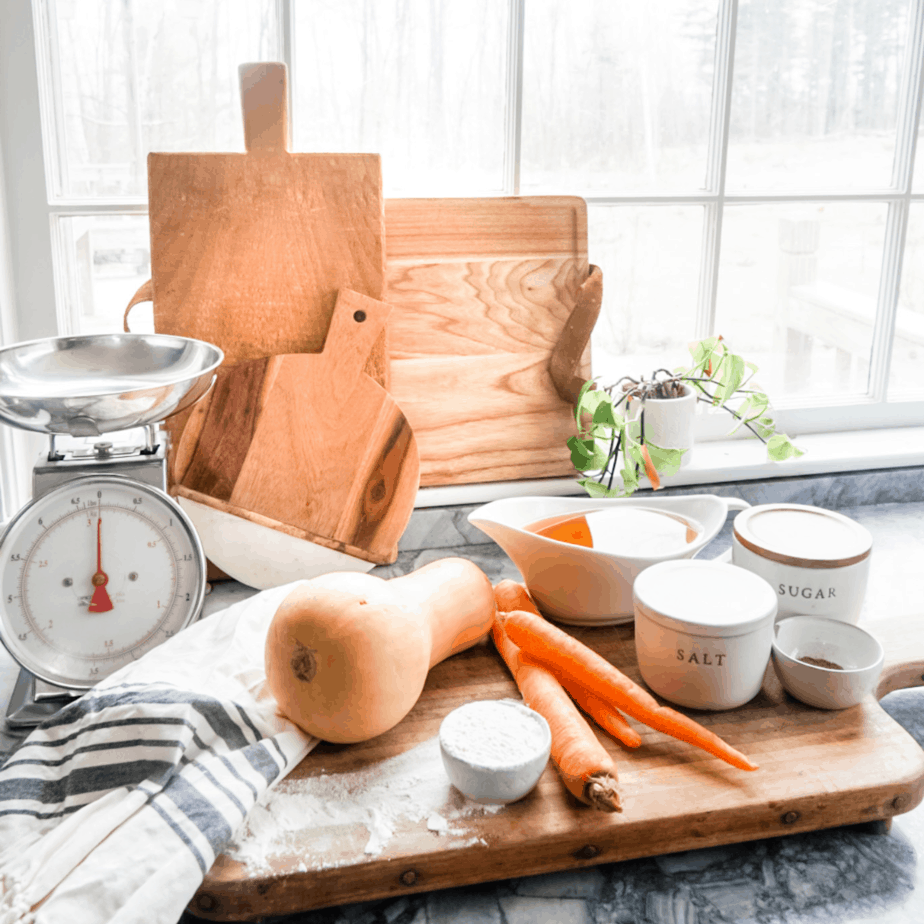 A wooden cutting board with carrots, squash, salt, and a scale all laid out for the soup.