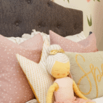 Little girl stuffed doll with pink pillows on white bedding