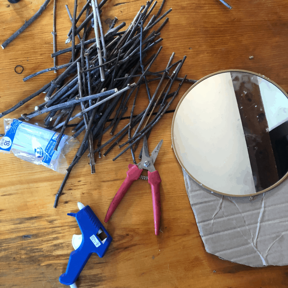 Round mirror, sticks, hot glue gun and shears laid out for the tutorial.