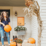 woman holding pumpkin o front porch with orange fall sign