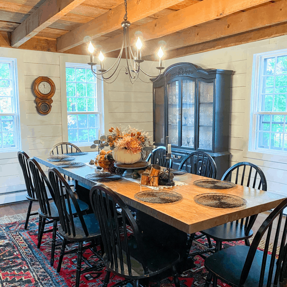 farmhouse dining room with red rug, large table, black chairs, and black light fixture