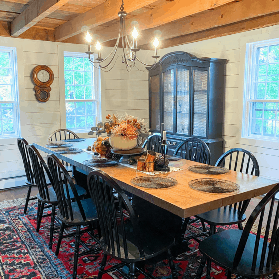 boho farmhouse dining room with large wooden table and wooden exposed beams. Pumpkin floral centerpiece on a cake stand on the table and a red boho farmhouse rug on the floor.