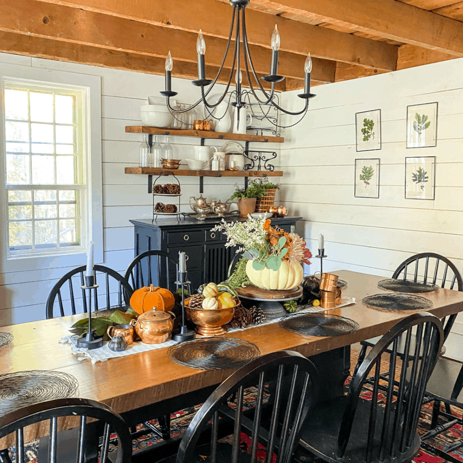 large dining room table with pumpkins in centerpiece, large exposed beams, and open shelving with kitchen are on shelf