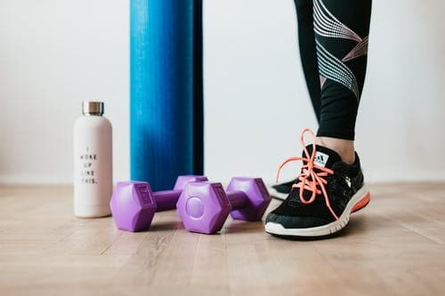 woman in black leggings and black sneakers with dumbbells and a water bottle.