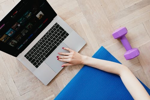 woman with dumbells, laying on a yoga mat, looking for a workout on the computer. 
