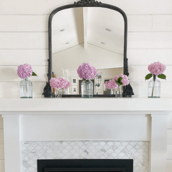 white fireplace mantel with pink flowers in glass jars.