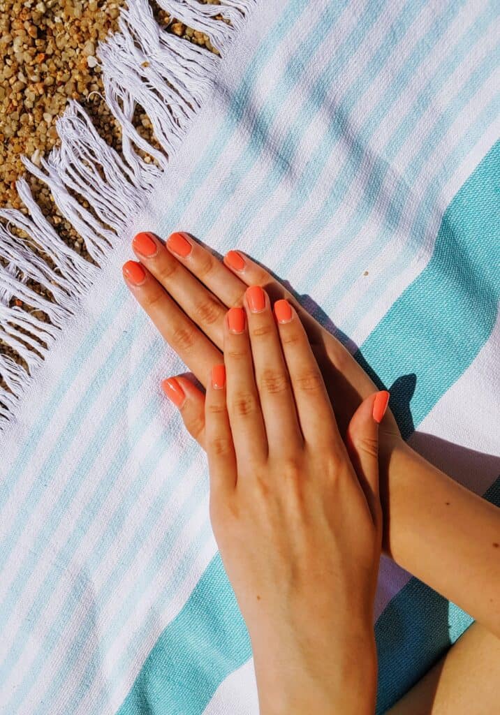 Woman two hands stacked on top of one another on top of a blue stripped towel with manicured pink nails.
