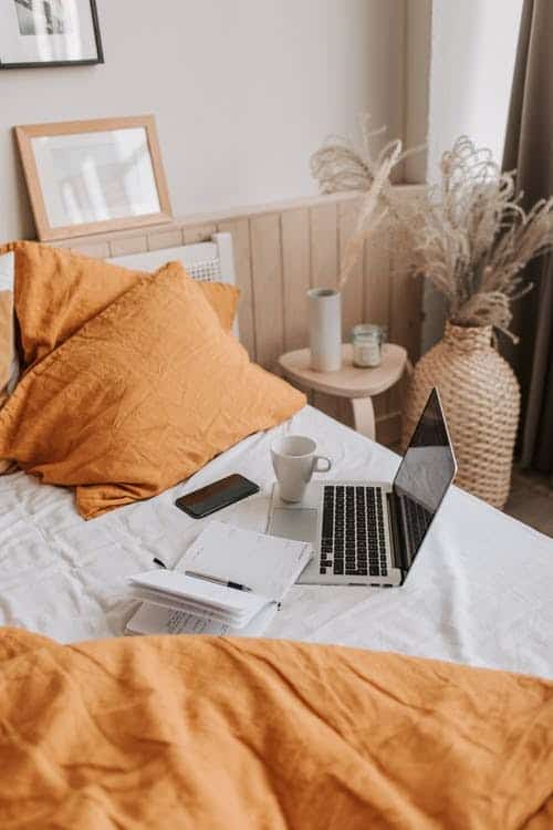 computer sitting on bed with orange bedding