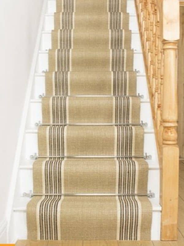 woven carpet runner with silver metal rods to hold carpet in place on stairs.