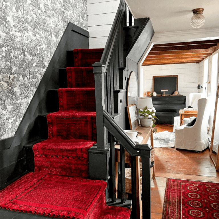 Toile wallpaper on wall up a staircase with a red runner and shiplap.