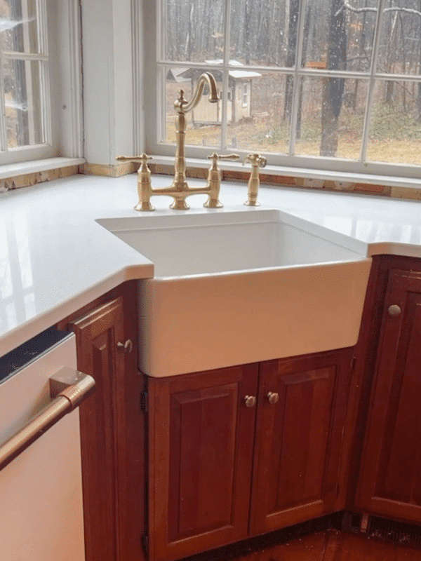 White farmers sink with gold faucet in maple corner retrofitted cabinet.