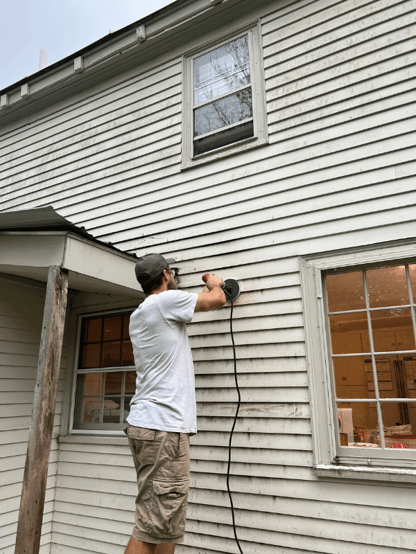 Man cutting hole in the side of the siding to install a vent hood.