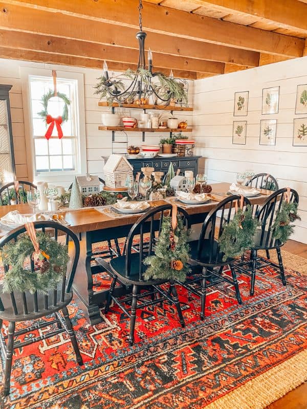 Christmas dining room table with farmhouse rwreaths on chairs and Christmas garland on table.