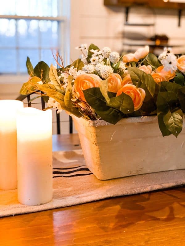 Flowers in planter and candles as a centerpiece on a dining room table.
