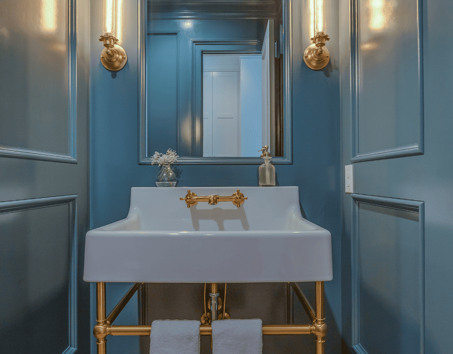 white pedestal sink in a bathroom with blue walls and gold fixtures. 