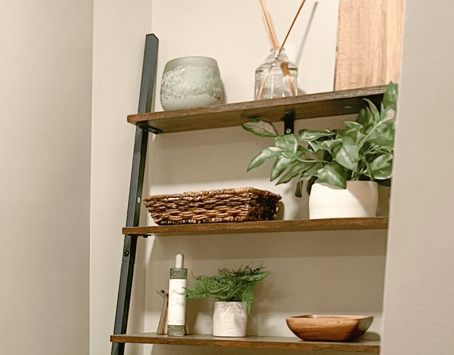 shelves above a toilet styled with plants and candles.